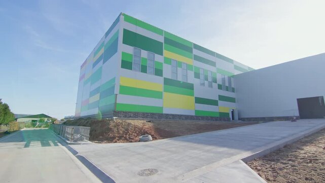 Spacious logistics facility with colorful sandwich wall panels. Paved concrete ramp leads toward building entrance alongside earthwork