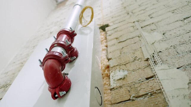 Fire suppression with heavy red couplings attaches beside raw masonry wall. Mechanical fittings installed during active wall preparation