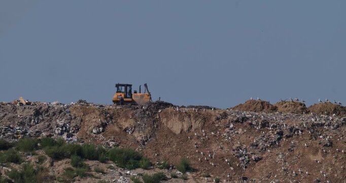 Bulldozer and unrecognizable operator working on municipal solid waste landfill site with atmospheric heat shimmer slow motion