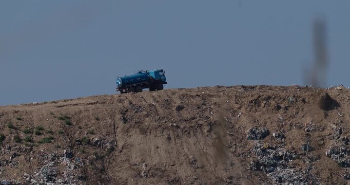 Distant view of blue vacuum tanker truck parked on top of MSW landfill site with atmospheric heat shimmer slow motion