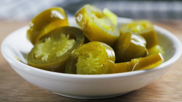 Sliced pickled jalapeno peppers served in a white bowl on a wooden table.