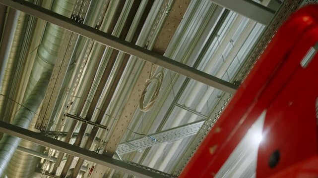 Network of utility pipes insulated lines and metal cable trays. Lift structure frame cuts across foreground of industrial ceiling layout