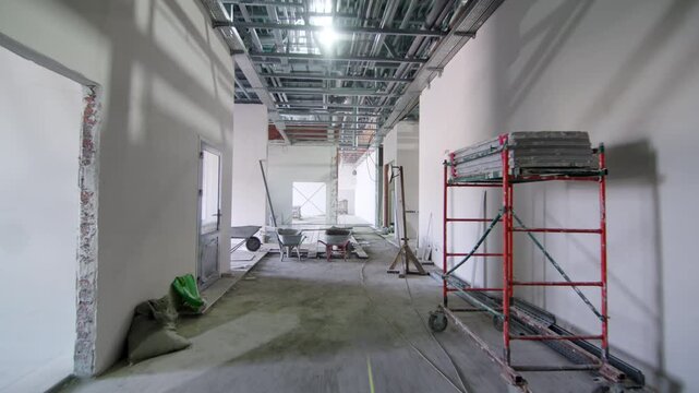 Mobile scaffold tower and construction materials line wide passageway. Ongoing finishing work proceeds along clean concrete floor pathway