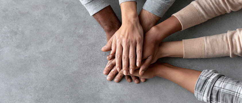 Overhead closeup of multiracial hands joined in solidarity, ideal for campaigns on inclusion, community, teamwork, and corporate diversity initiatives. Neutral concrete background adds.