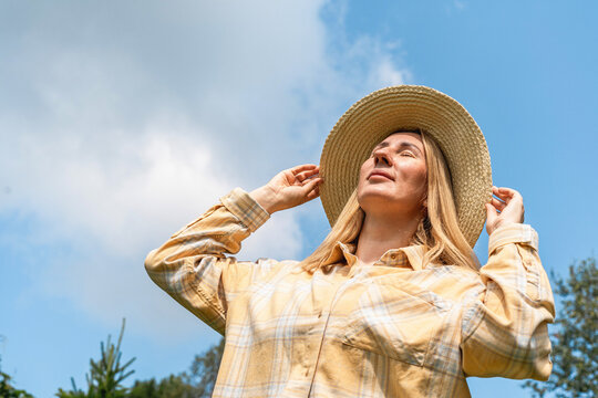 Woman standing outdoors, closing eyes, and embracing the warm sunlight on her face. Feeling relaxed and peaceful in nature