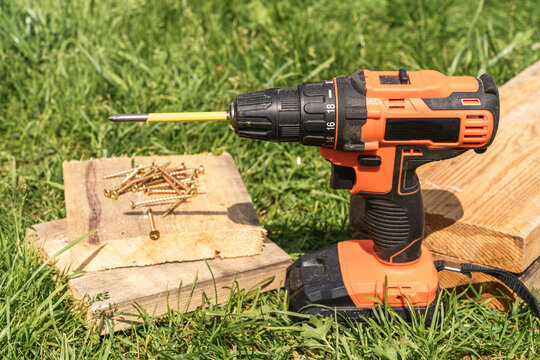 Cordless drill, screws, and wooden planks on grass, representing home improvement, construction, and carpentry