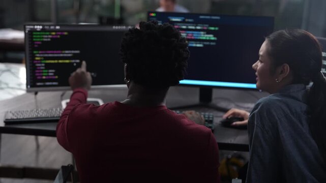 Diverse software developer team coding on computer monitors. Smiling Asian female programmer discussing IT projects with African American colleague. Corporate technology, and modern teamwork concepts