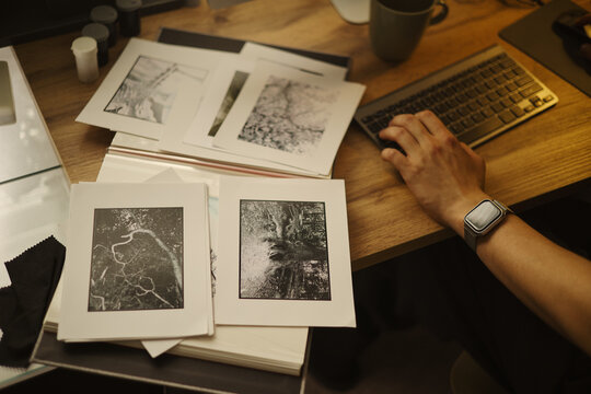 Male photographer hand typing on keyboard next to printed black and art photos, organizing portfolio. Image suitable for creative agency or art gallery marketing