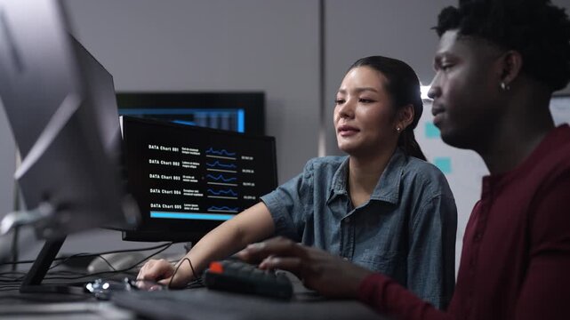 Diverse software developer team coding on computer monitors. Smiling Asian female programmer discussing IT projects with African American colleague. Corporate technology, and modern teamwork concepts