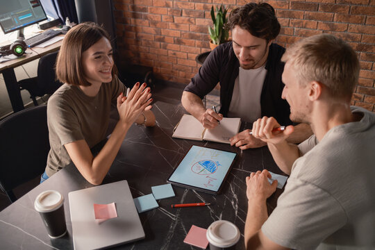 Three colleagues brainstorming ideas with tablet and notes in creative workspace