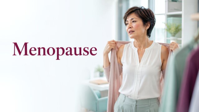 Middle-aged Asian woman in light blouse adjusting her cardigan, standing in a bright room with clothing racks, emphasizing menopause and its impact on daily life