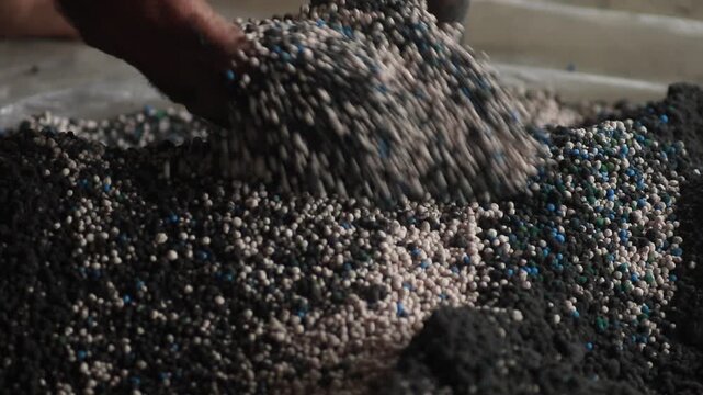 Close up of farmer rough hands mixing colorful NPK fertilizer granules with black organic peat powder
