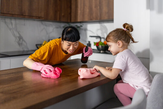 Mother and daughter cleaning kitchen table together sharing a playful household moment