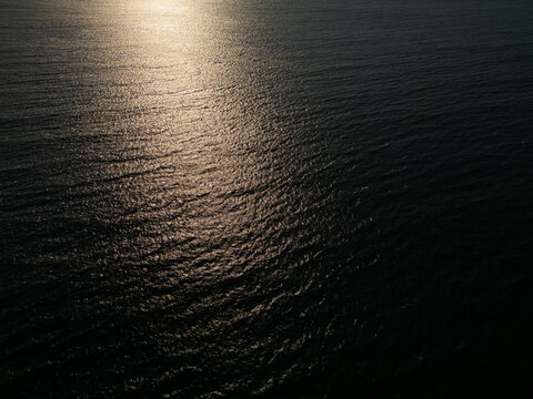 Aerial View of Calm Ocean Water Surface with Golden Sun Reflection at Sunset