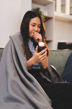 sick asian young woman sneezing into tissue paper while covered with a blanket and sitting on sofa in the living room