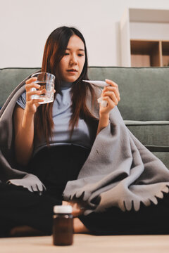 sick asian young woman sneezing into tissue paper while covered with a blanket and sitting on sofa in the living room