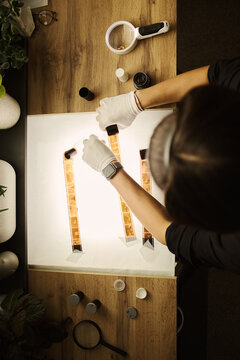 High angle view of young Caucasian woman wearing gloves and examining analog film strips on light table, representing photography archiving and restoration services, vertical