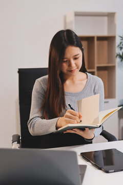 Young asian businesswoman is smiling and working on a laptop while sitting at her desk in a modern office