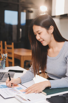 Young asian businesswoman is smiling and working on a laptop while sitting at her desk in a modern office