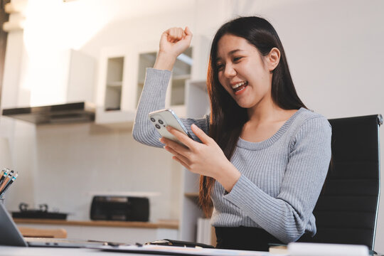 Young asian businesswoman is smiling and working on a laptop while sitting at her desk in a modern office