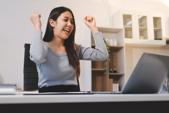 Young asian businesswoman is smiling and working on a laptop while sitting at her desk in a modern office