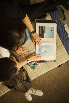 High angle view of young couple looking at photo album together, reminiscing about travel memories. Image is suitable for family lifestyle and print service marketing, vertical