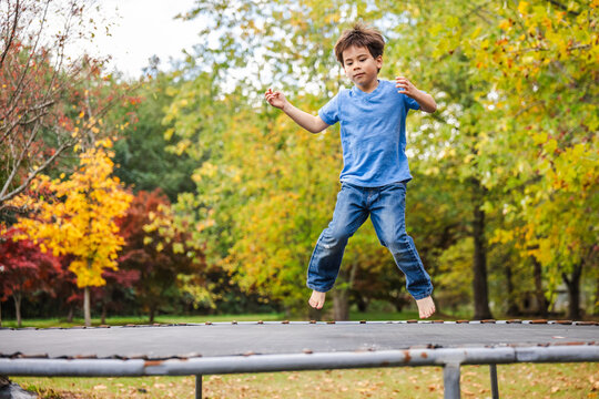 Young Boy Jumping on Trampoline Among Autumn Trees