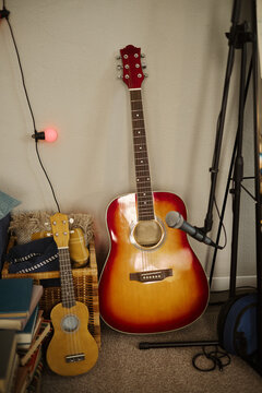 Acoustic guitar and ukulele leaning against wall next to microphone on stand in home studio. Image ideal for promoting music lessons, creative hobbies, or audio recording, vertical