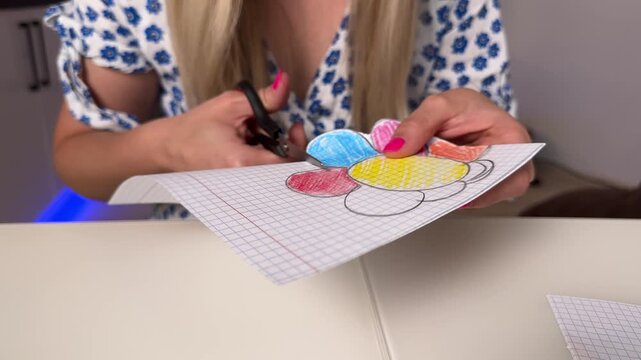 Close-up hands cutting colored paper flower on countertop for DIY craft tutorial, with cutting, craft, hand, scissor detail, showing paper, flower, drawn, coloring context
