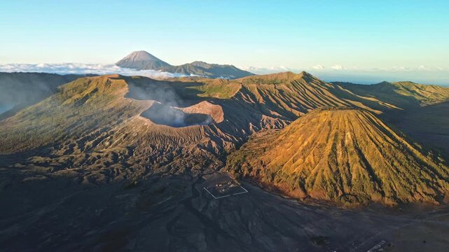 Drone slowly orbits the Mount Bromo volcanic landscape in vibrant golden-yellow morning light, revealing volcanic peaks, deep shadows and a clear blue sky, Indonesia
