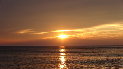 Fototapeta premium Brilliant Golden Sunrise Reflecting on Ocean Waves. Intense golden sunlight piercing through dark clouds at sunrise, creating a sparkling sun trail across the rippling sea surface.