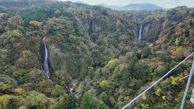 Scenic waterfalls flow through a lush mountain valley in autumn.