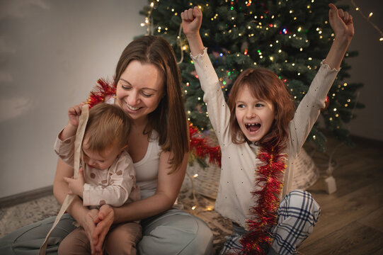 Mother and daughters opening presents under the tree, New Year and Christmas celebrations. Gift wrapping real people, real emotions