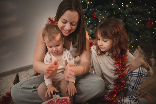 Mother and daughters opening presents under the tree, New Year and Christmas celebrations. Gift wrapping real people, real emotions