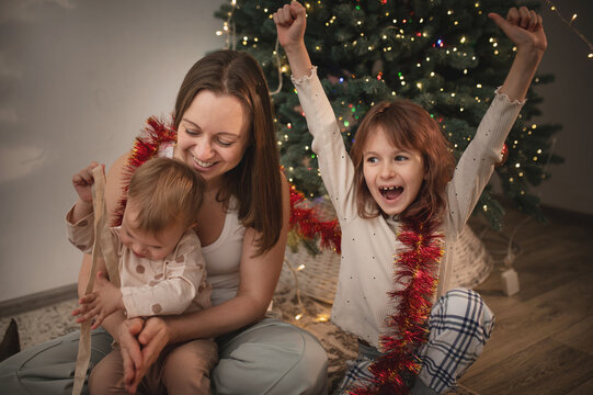 Mother and daughters opening presents under the tree, New Year and Christmas celebrations. Gift wrapping real people, real emotions