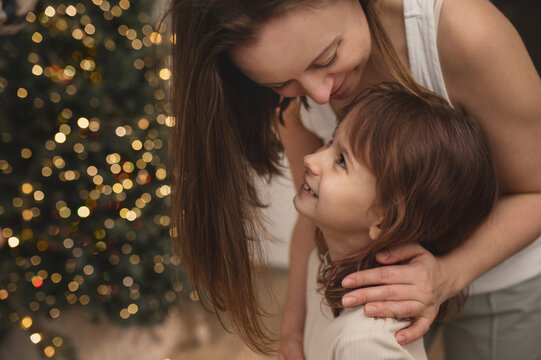 portrait of mother and daughter, real people, hugging in front of Christmas tree, celebrating Christmas. out of focus, moving with noise and scratches on the sensor, blurring. vibrant, emotional photo
