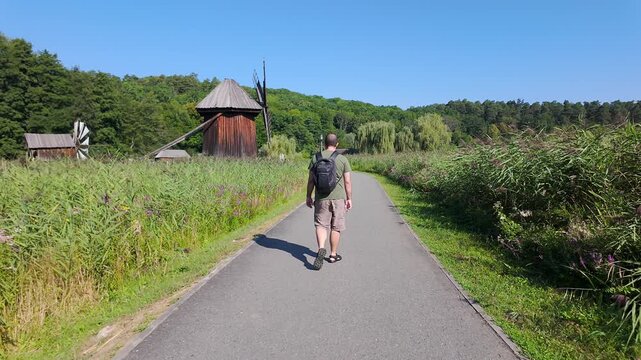 Male tourist walking along a rural path toward traditional wooden windmills in Romania