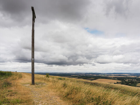 Combe Gibbet stands beside a grassy ridge path overlooking panoramic views of the Kennet Valley under dramatic clouds in Berkshire, UK