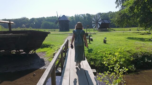 Woman tourist crossing a wooden footbridge toward traditional rural windmills in Romania