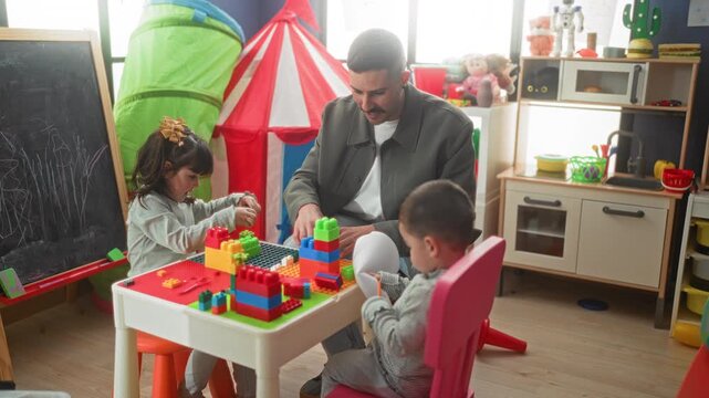 Man assembles toy block tower with children at play table in a building; playful learning warmth together.