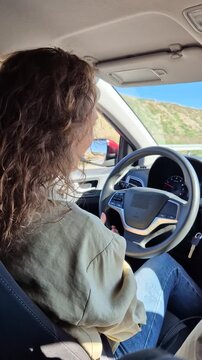 Woman driver navigating scenic coastal highway road in sunny weather during daytime travel. Static medium shot from the passenger seat perspective.