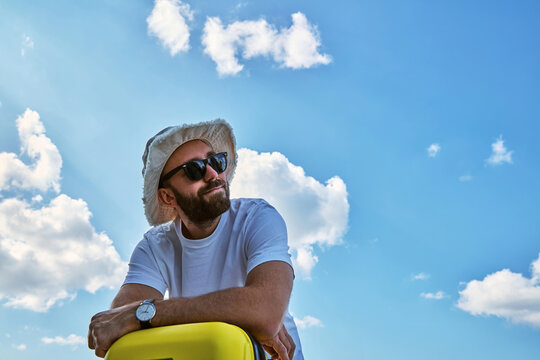 Happy Man with Yellow Suitcase Against Blue Sky During Summer Travel