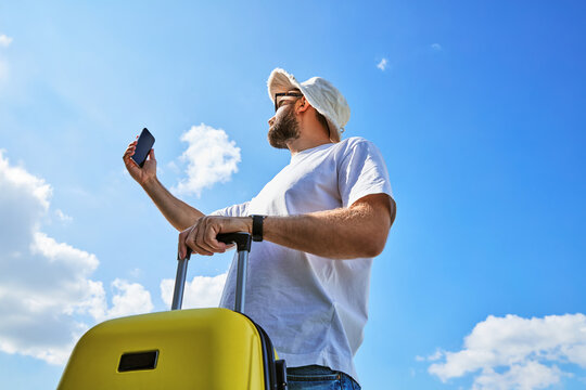 Low Angle View of Man Traveler with Yellow Suitcase Taking Selfie against Blue Sky