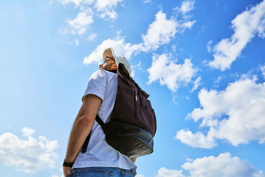 Low Angle View of Young Male Traveler with Backpack Looking at Blue Cloudy Sky