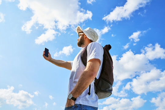 Young Backpacker Taking Selfie with Smartphone Against Blue Sky