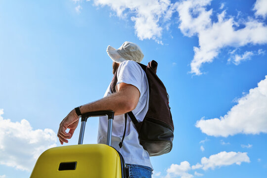Male traveler with backpack and yellow suitcase against blue sky