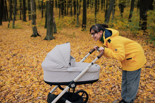 Young mother walking with baby stroller in autumn forest