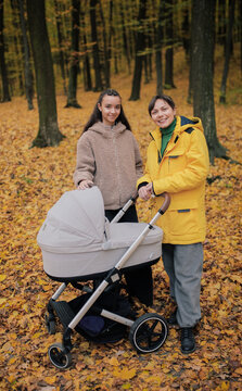 Mother and daughter walking with baby stroller in autumn forest