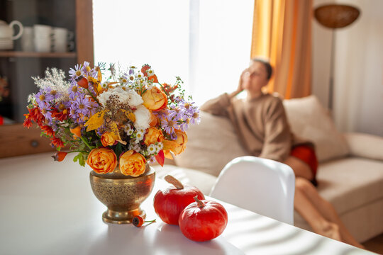 Fall interior decor of living room. Woman relaxing at home decorated for autumn with bouquet of flowers, pumpkins. Thanksgiving