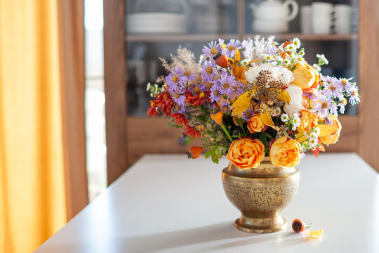 Floral arrangement in brass vase. Fall interior decor of living room. Home decorated for autumn with bouquet of rose aster flowers